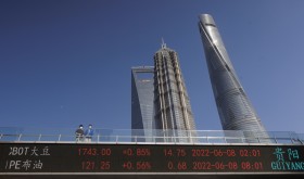 People stand on pedestrian bridge showing stock exchange data in Lujiazui